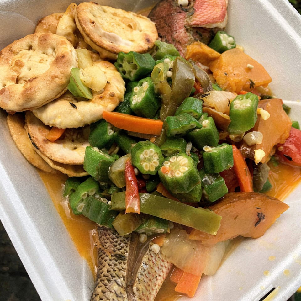 Curly's Caribbean steamed fish with okra, carrots, and bammy in a takeout container.