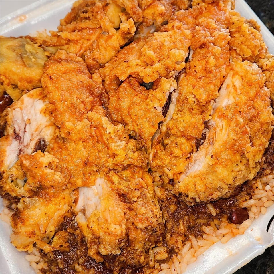 Crispy fried chicken pieces served over rice and beans in a white takeout container from Curly's Caribbean.
