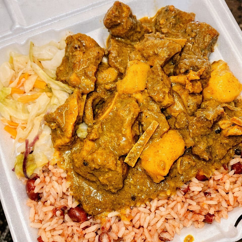 Curry goat with rice and peas, and steamed cabbage in a white takeout container from Curly's Caribbean.