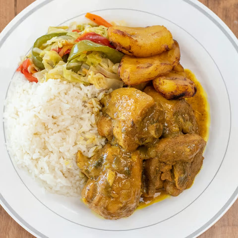 A plate of Curly's Caribbean curry chicken, white rice, steamed vegetables, and fried plantains.