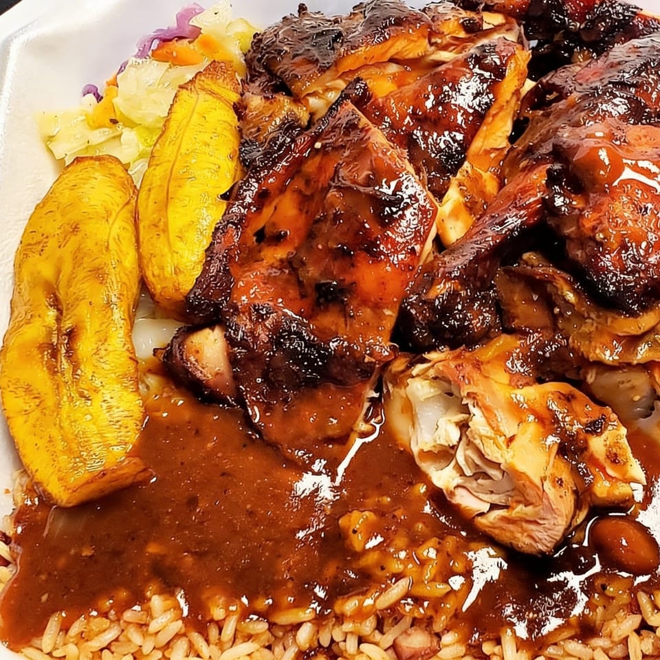 Close-up of Curly's Caribbean jerk chicken with plantains, rice, beans, and cabbage.